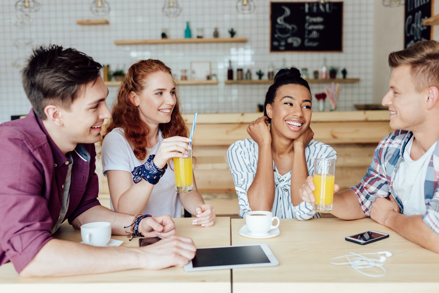 Un grupo de amigos tomando jugo de naranja y café o té en una tienda mientras hablan de cosas, tal vez un podcast.