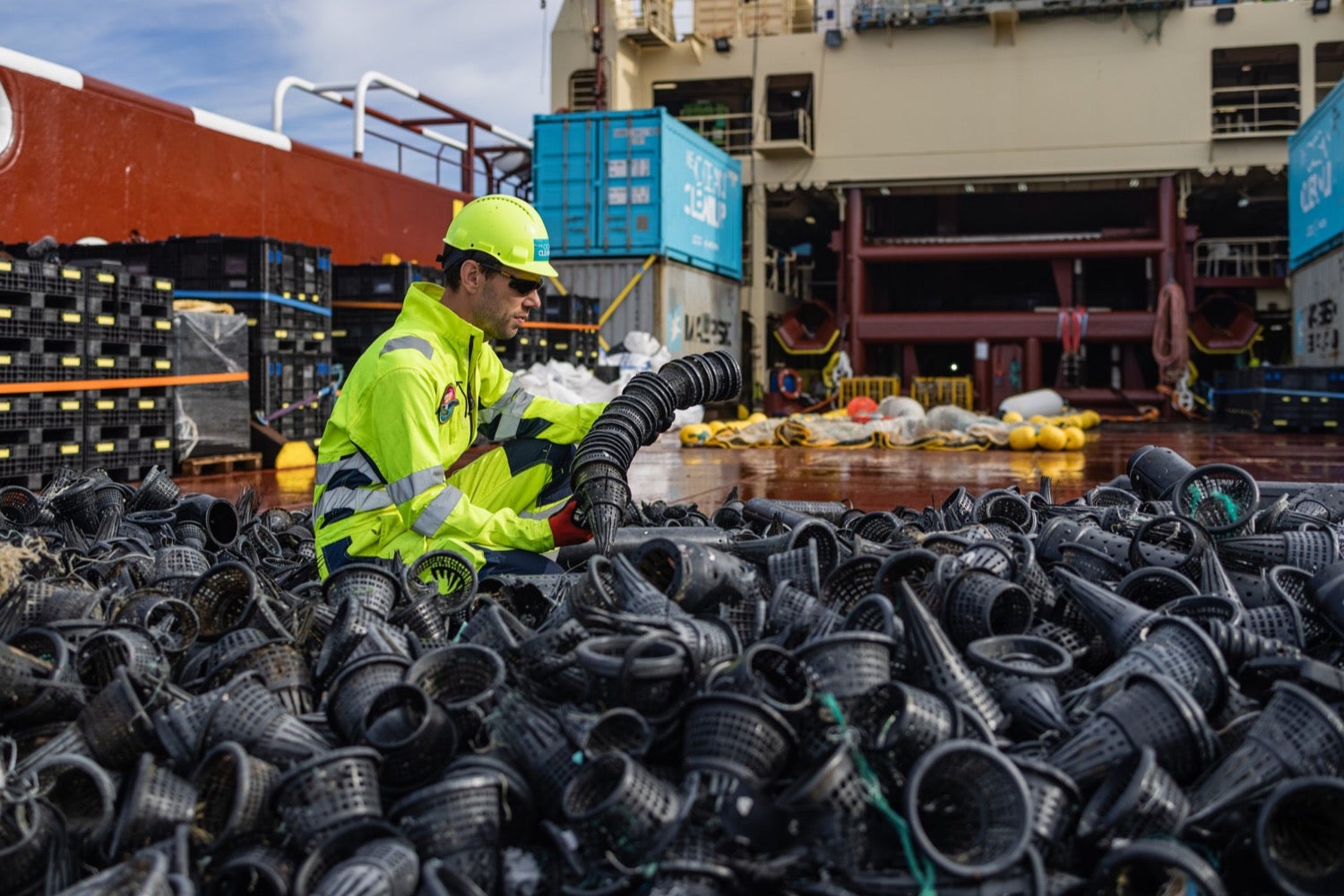 Un hombre con un traje de trabajo de materiales peligrosos amarillo apila conos de plástico negro en un barco