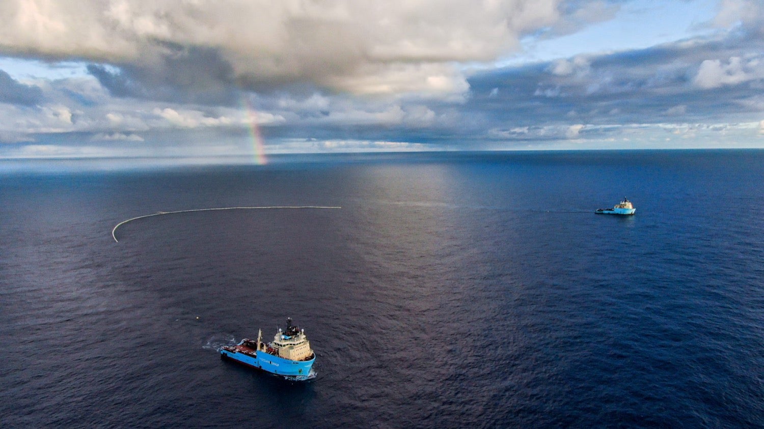 Dos barcos tiran a lo largo de una barrera en forma de U a través del mar